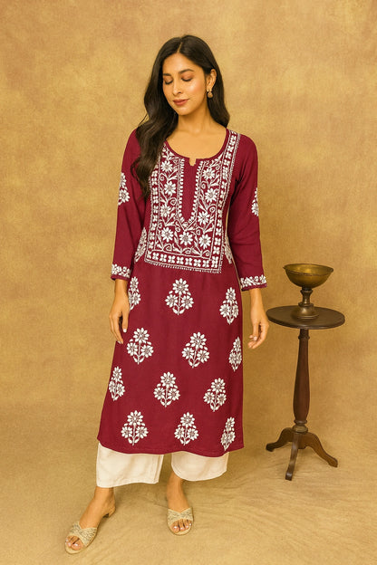 Woman wearing a maroon embroidered kurta with white pants against a beige background