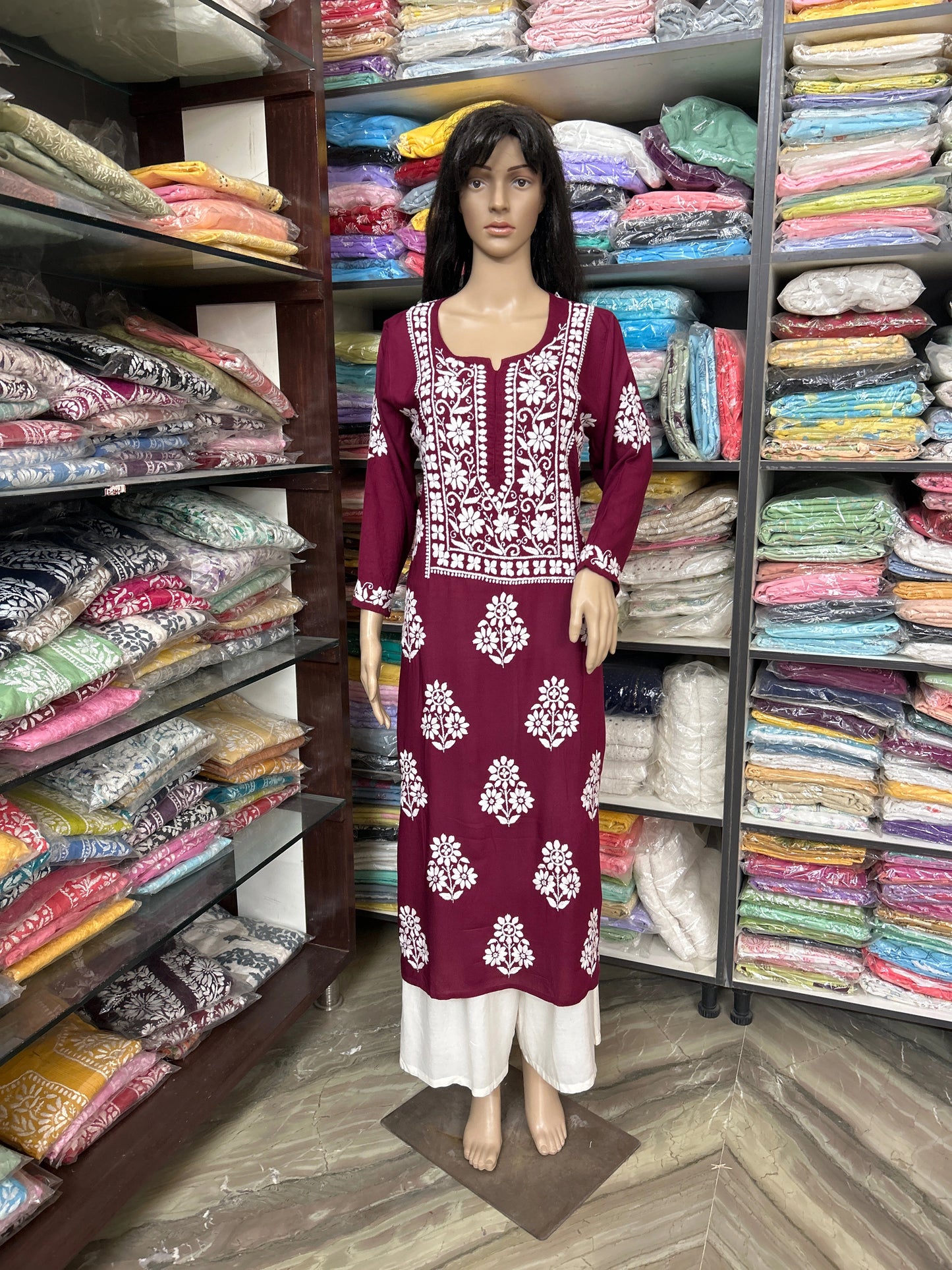 Mannequin wearing a maroon dress with white patterns in a fabric store.