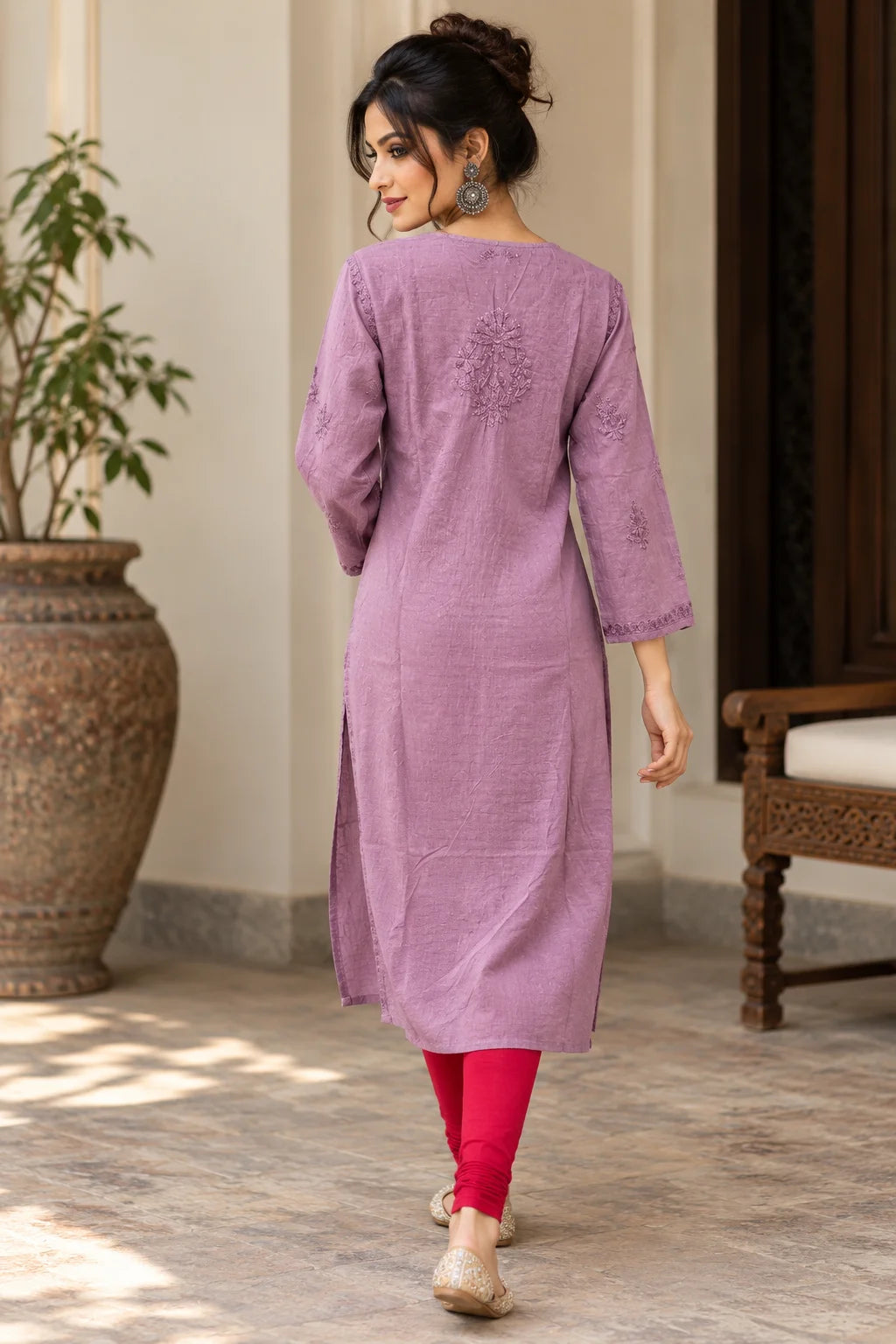 A woman wearing a lavender purple cotton kurta with floral embroidery on the back, paired with bright pink leggings and beige flat shoes, walking in a courtyard setting.