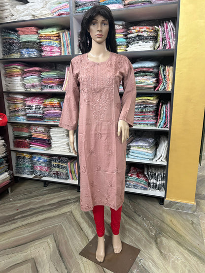 A mannequin wearing a dusty pink embroidered kurta with red leggings, standing in front of shelves filled with folded clothing in a retail store.