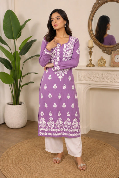 Woman wearing a purple and white embroidered outfit standing in a room with a mirror and plant.