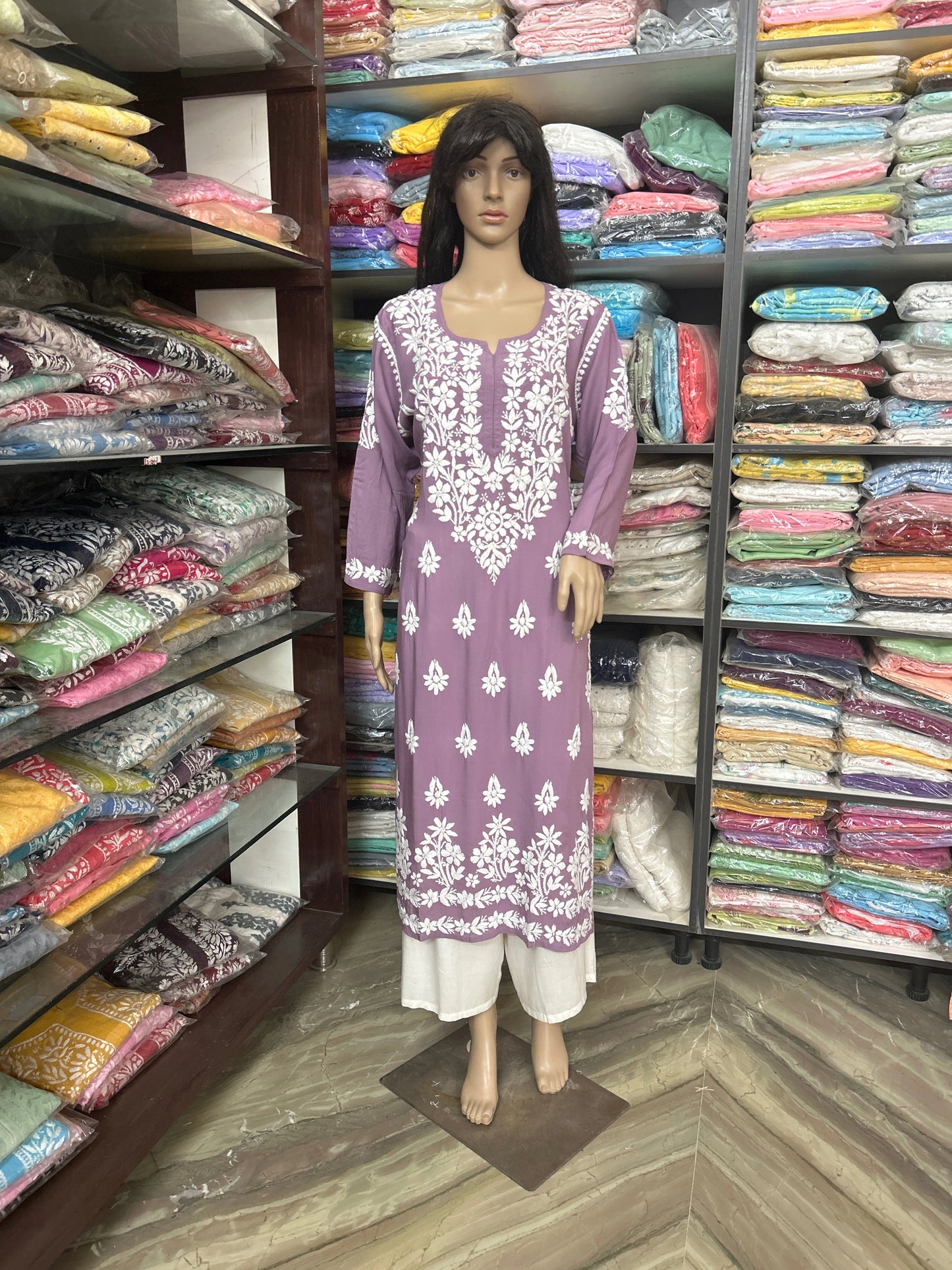 Mannequin wearing a purple embroidered kurta in a fabric store with shelves of colorful fabrics.