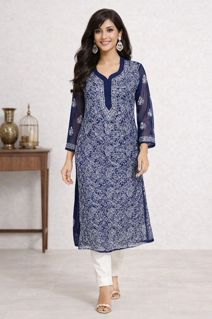 Lucknowi chikankari A woman modeling a navy blue and white printed kurta with white pants, standing in a studio setting with a decorative side table in the background.