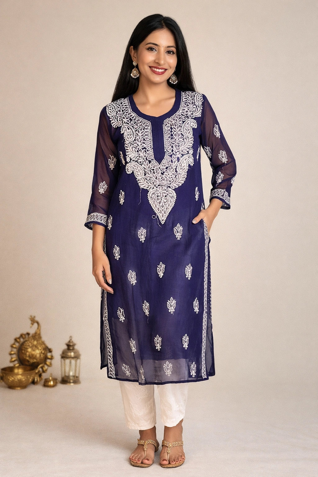 A woman modeling a navy blue embroidered kurta with white floral patterns and white pants, standing against a plain beige background.