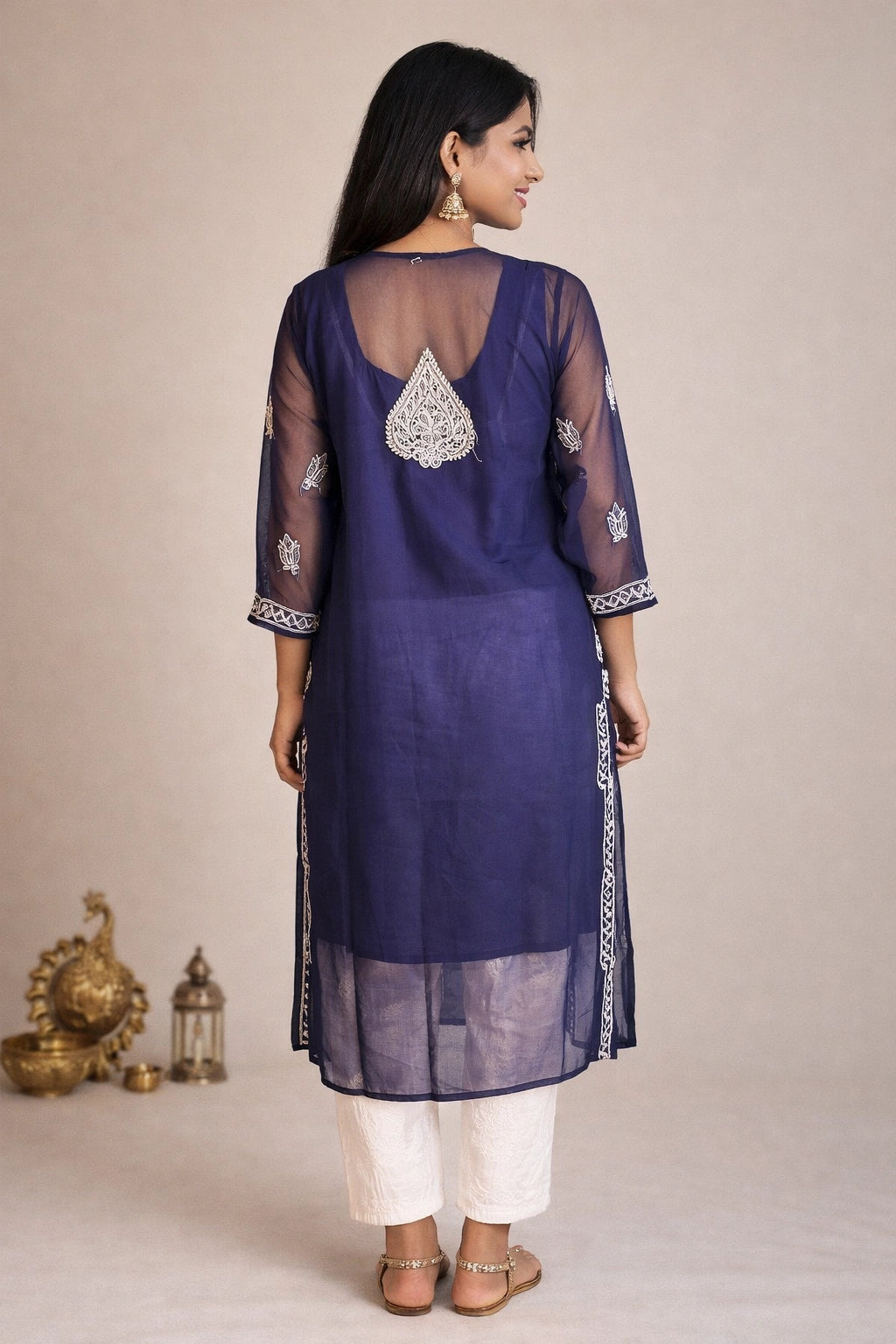 Lucknowi chikankari A woman is shown from the back wearing a deep purple kurta with silver embroidery, paired with white pants, against a neutral beige background.