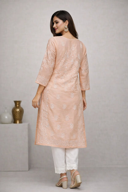 A woman modeling a peach-colored embroidered kurta with white pants and beige heels, shown from the back against a neutral gray studio background.
