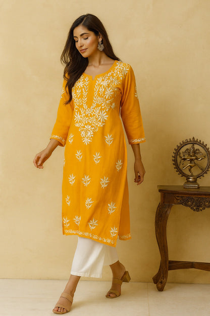 Woman wearing a yellow embroidered kurta with white pants against a beige background