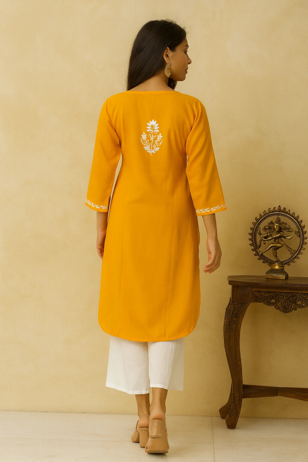 Woman wearing a yellow kurta with white embroidery, standing against a beige wall.
