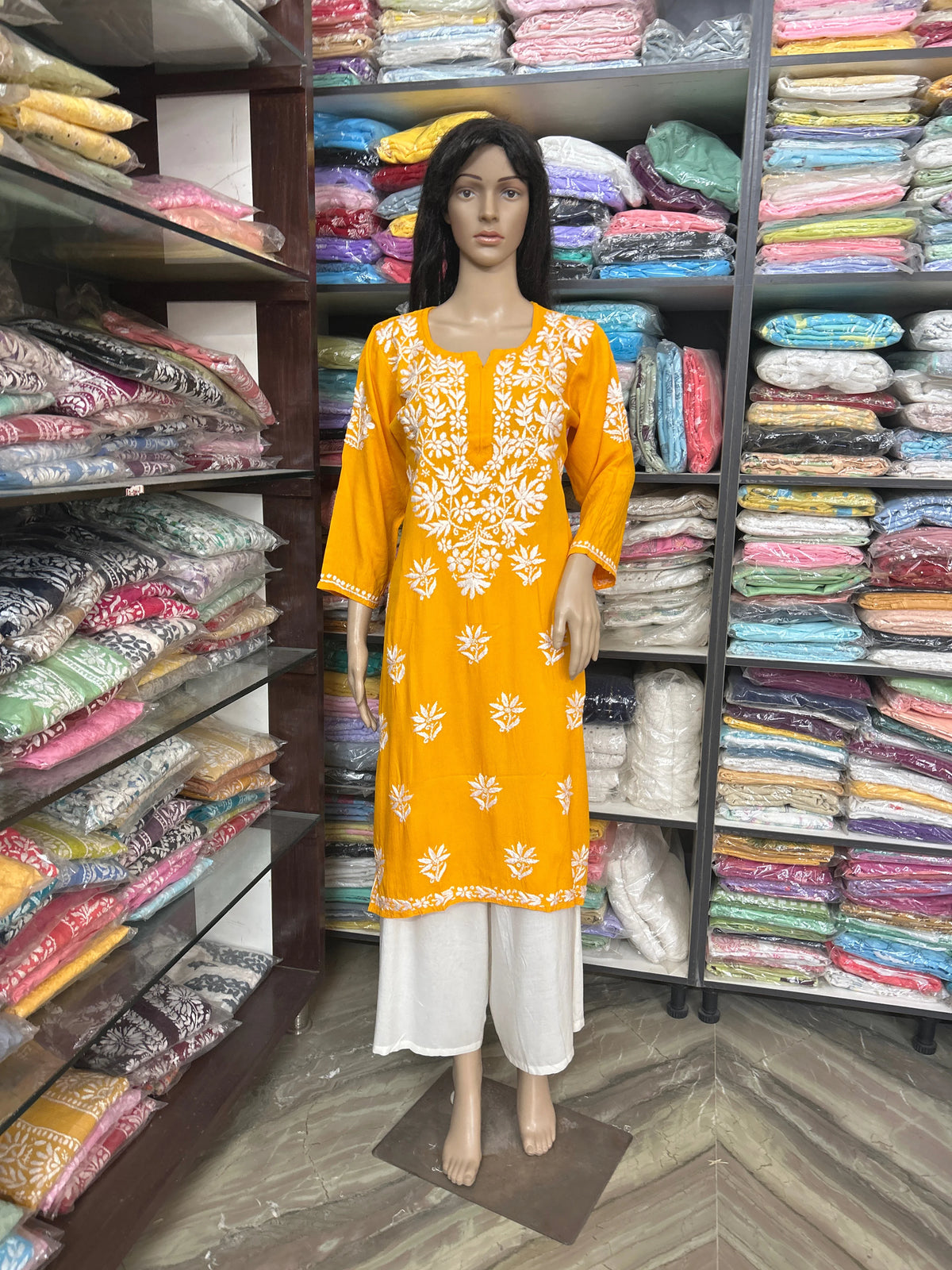 Mannequin wearing an orange and white embroidered dress in a fabric store.