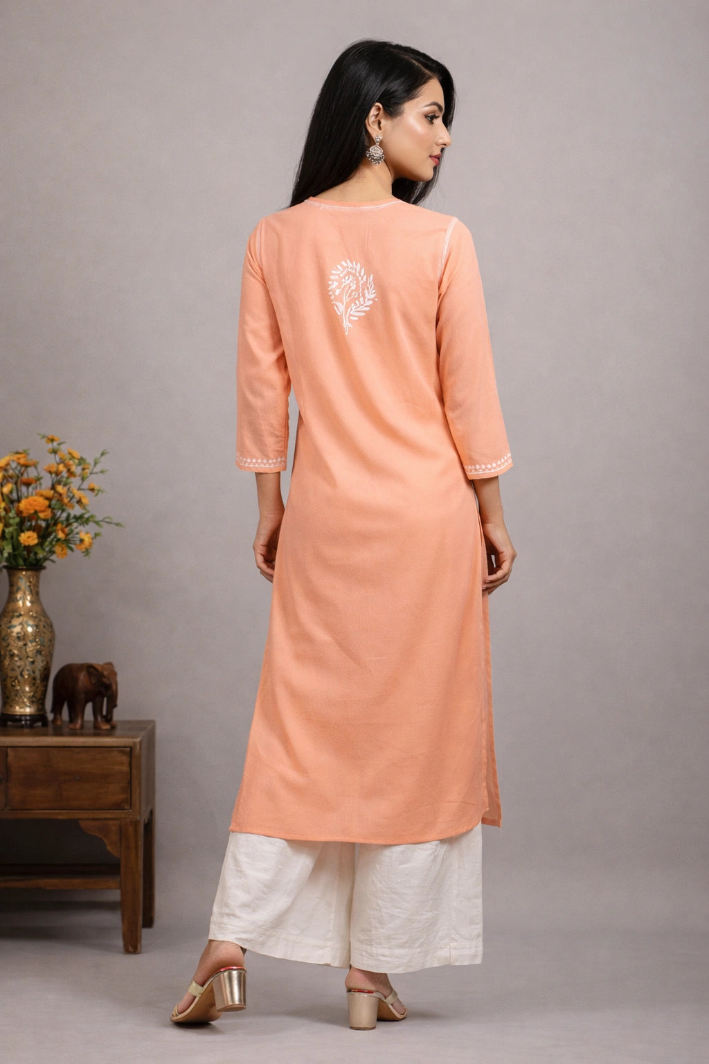 Woman wearing a peach kurta with white pants against a gray background