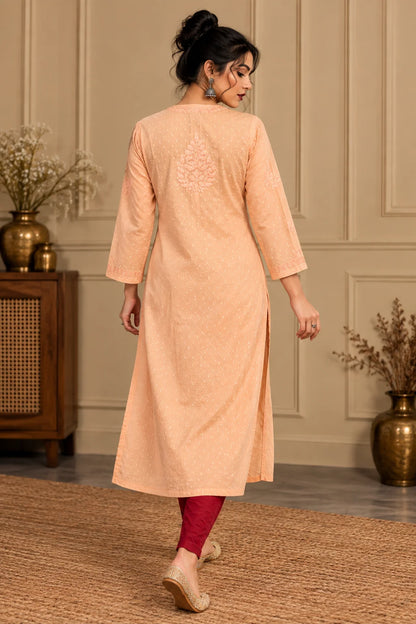 A woman wearing a peach-colored embroidered kurta with three-quarter sleeves and red leggings, shown from the back in a decorated indoor setting.