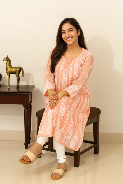 lucknowi chikankari Woman wearing a peach-colored kurta sitting on a wooden stool indoors.