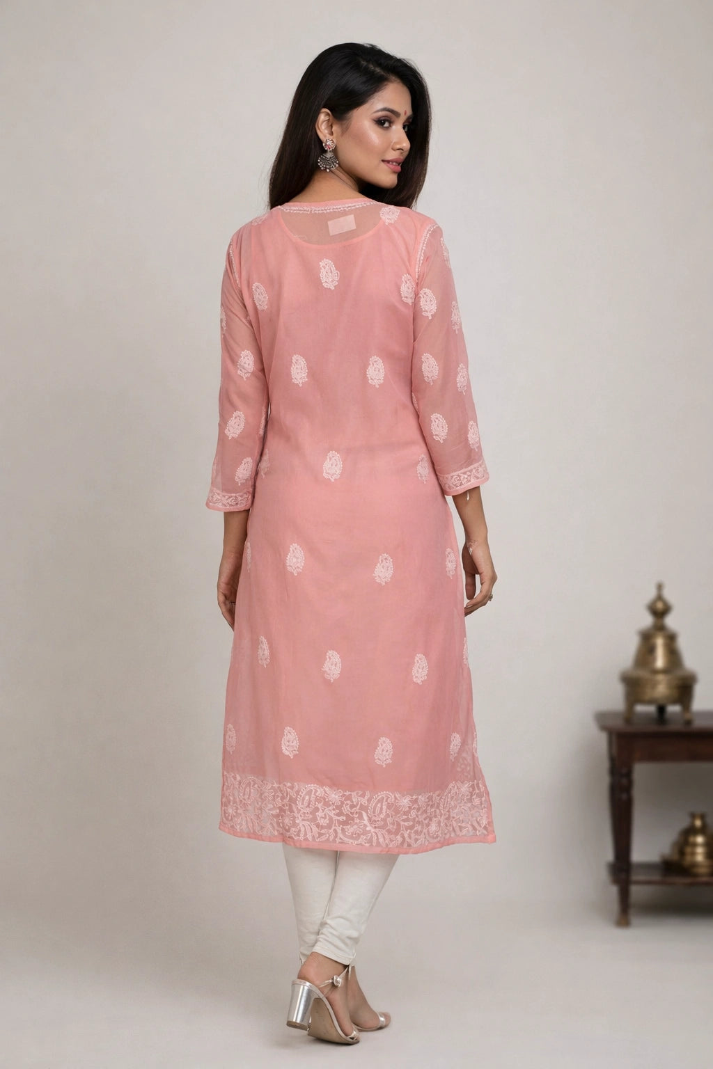 Woman wearing a pink kurta with white patterns against a plain background