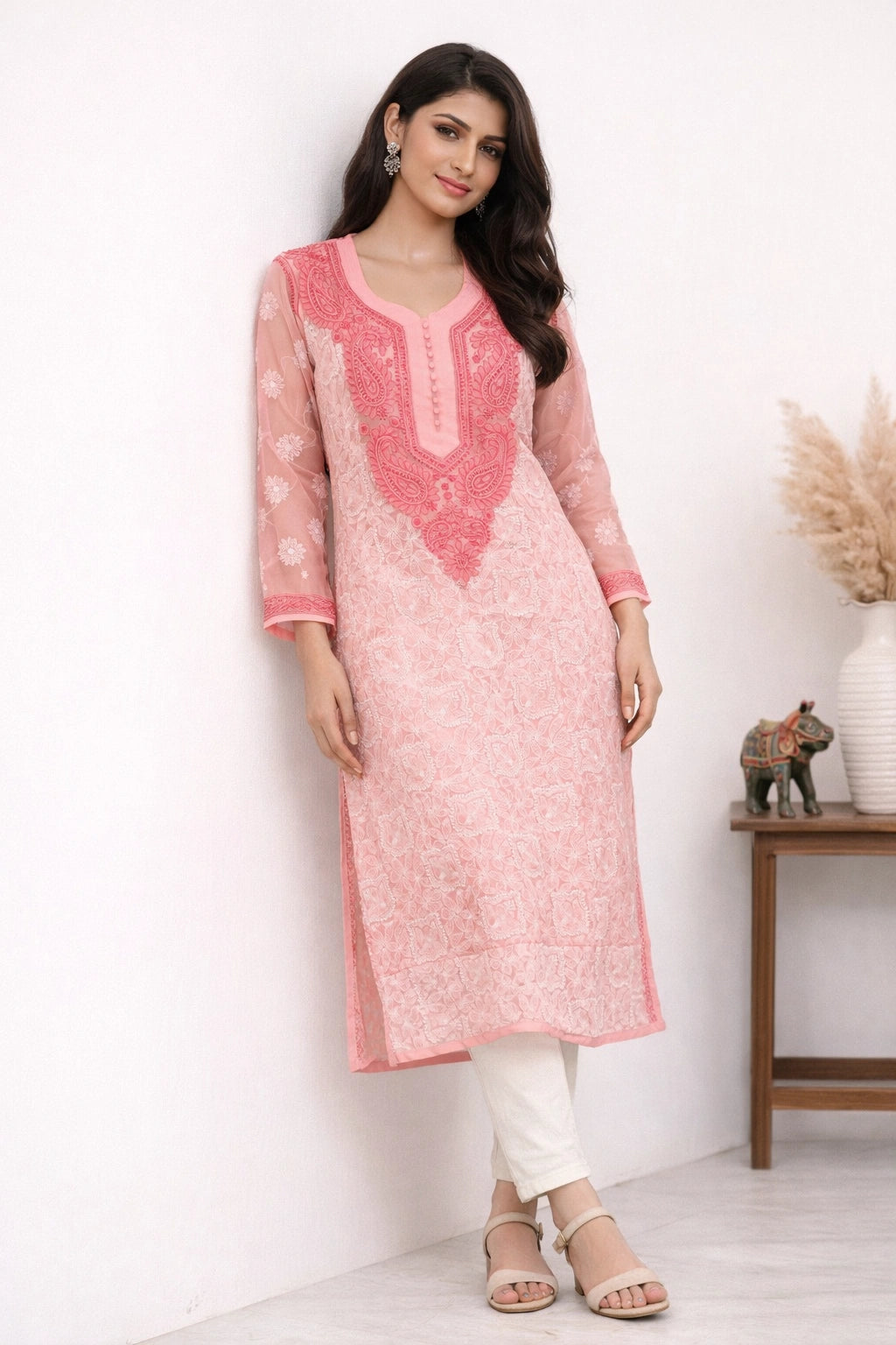 Woman wearing a pink embroidered kurta with white pants against a white background