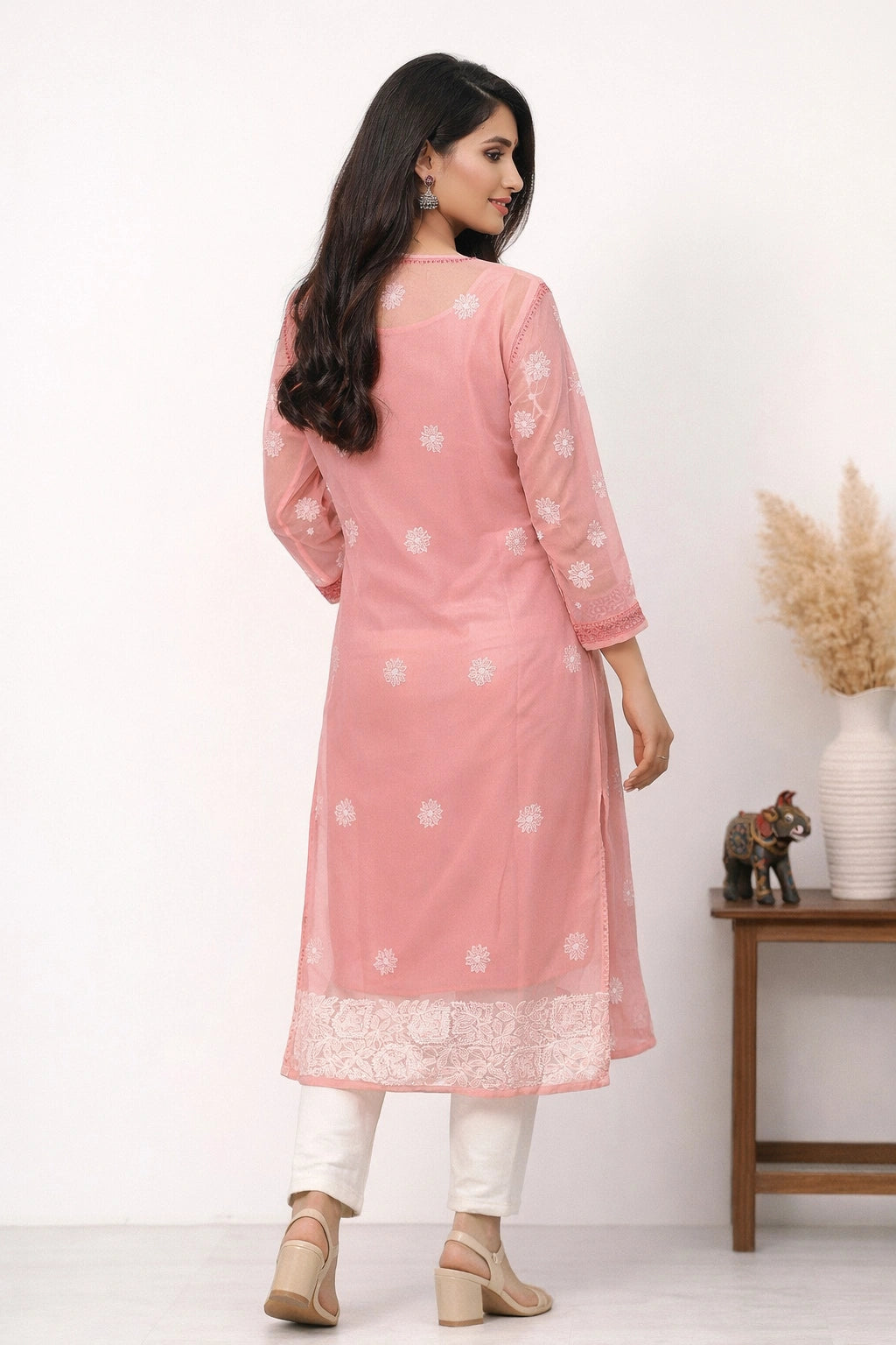 Woman wearing a pink traditional outfit with white patterns, standing against a white background.