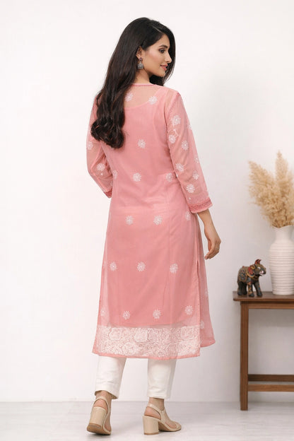Woman wearing a pink traditional outfit with white patterns, standing against a white background.