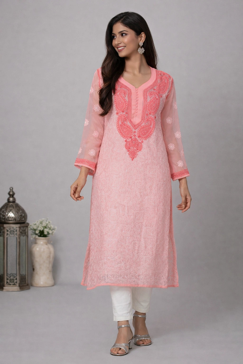 Woman wearing a pink embroidered kurta with white pants on a gray background
