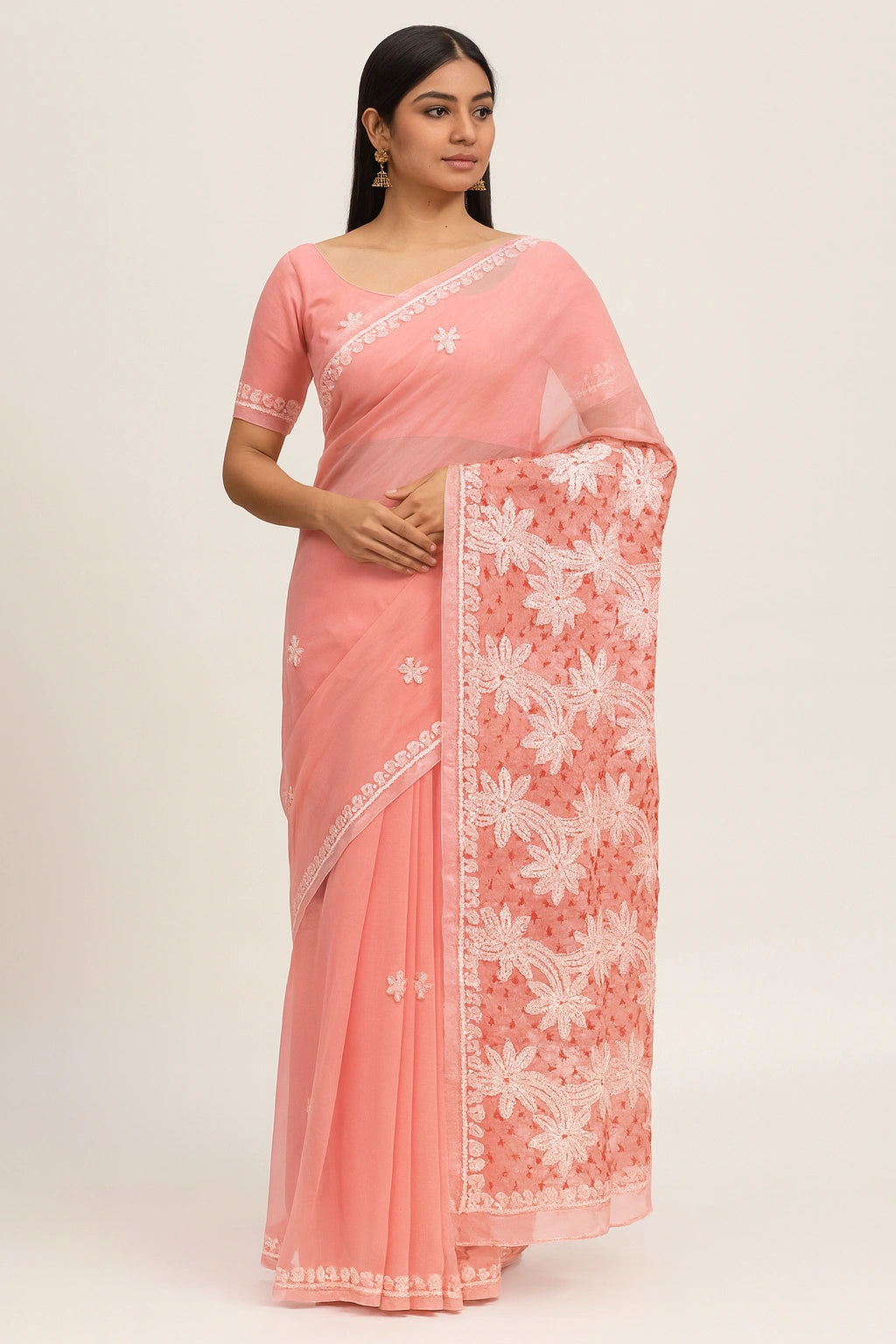 Woman wearing a pink saree with white floral embroidery on a plain background