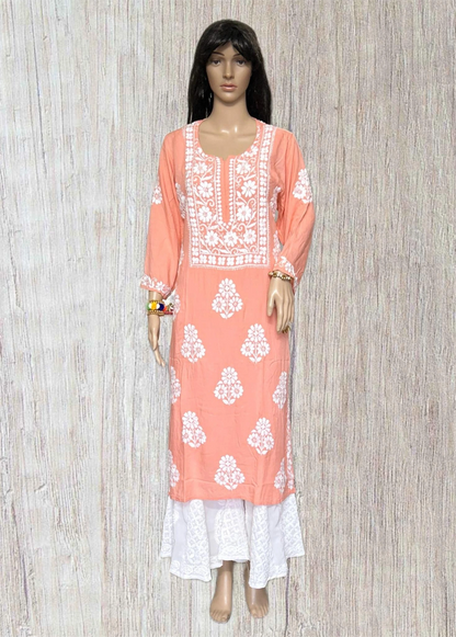 A peach-colored long kurta with white floral embroidery and white lace hem, displayed on a female mannequin against a light wood-textured background.