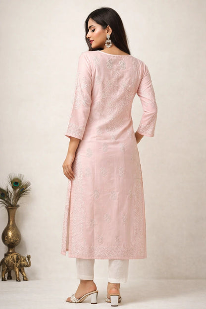 A woman modeling a light pink embroidered kurta with three-quarter sleeves, paired with white pants and silver heeled sandals, shown from the back against a neutral studio backdrop.