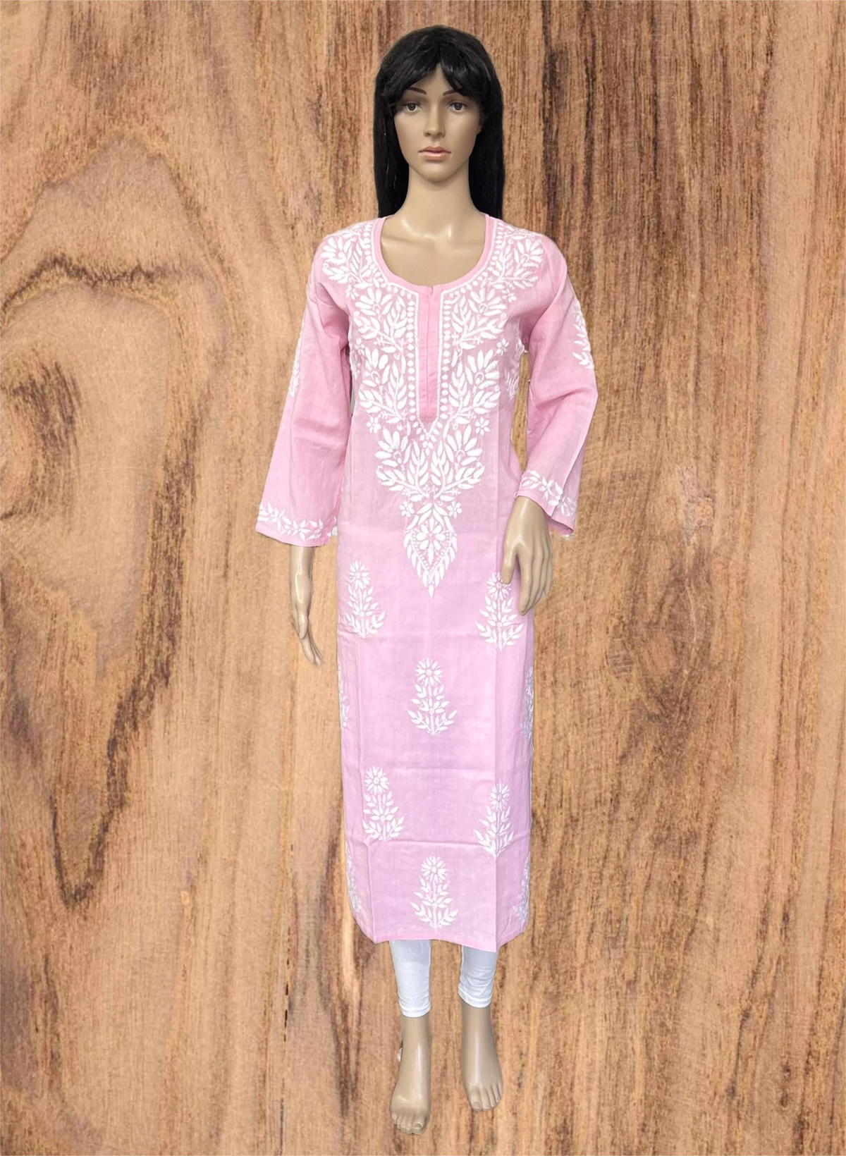 A pink long kurta with white floral embroidery displayed on a female mannequin against a wood-grain background.