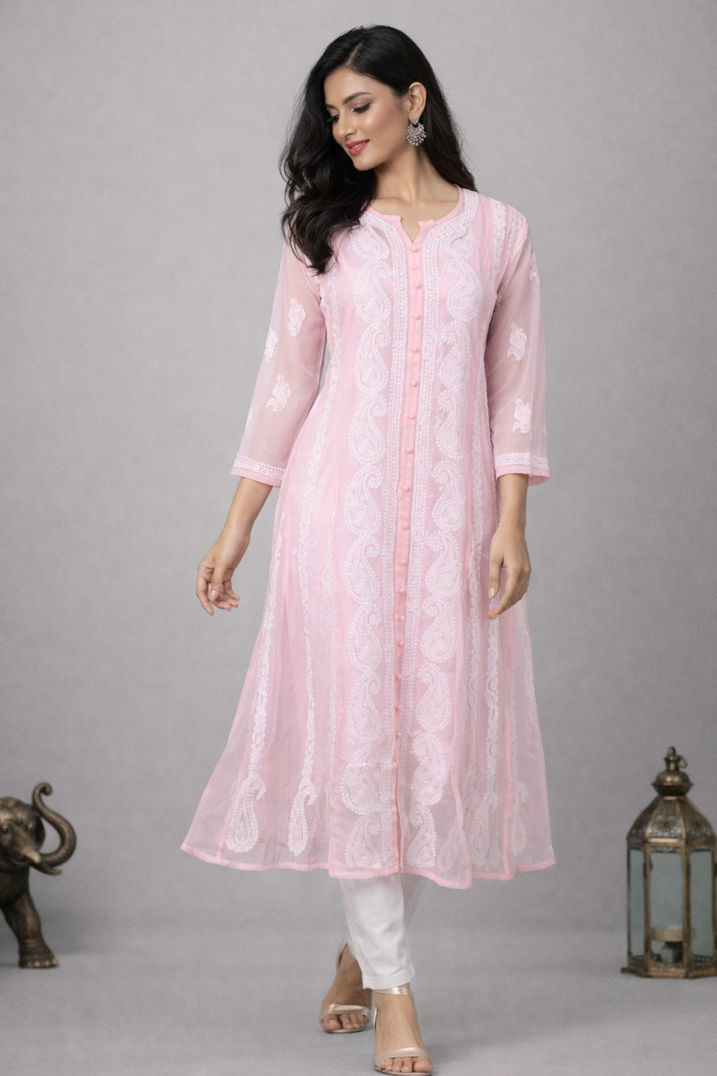 Woman wearing a light pink embroidered kurta with white pants on a gray background