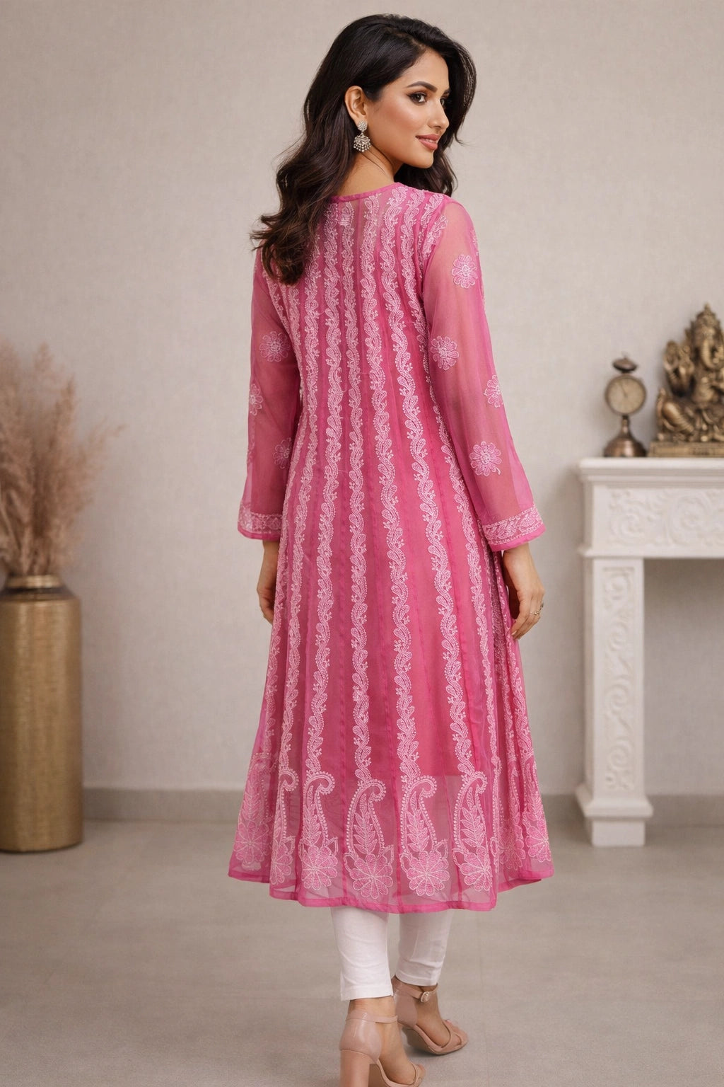 Woman wearing a pink traditional outfit with white patterns in a minimalistic setting.