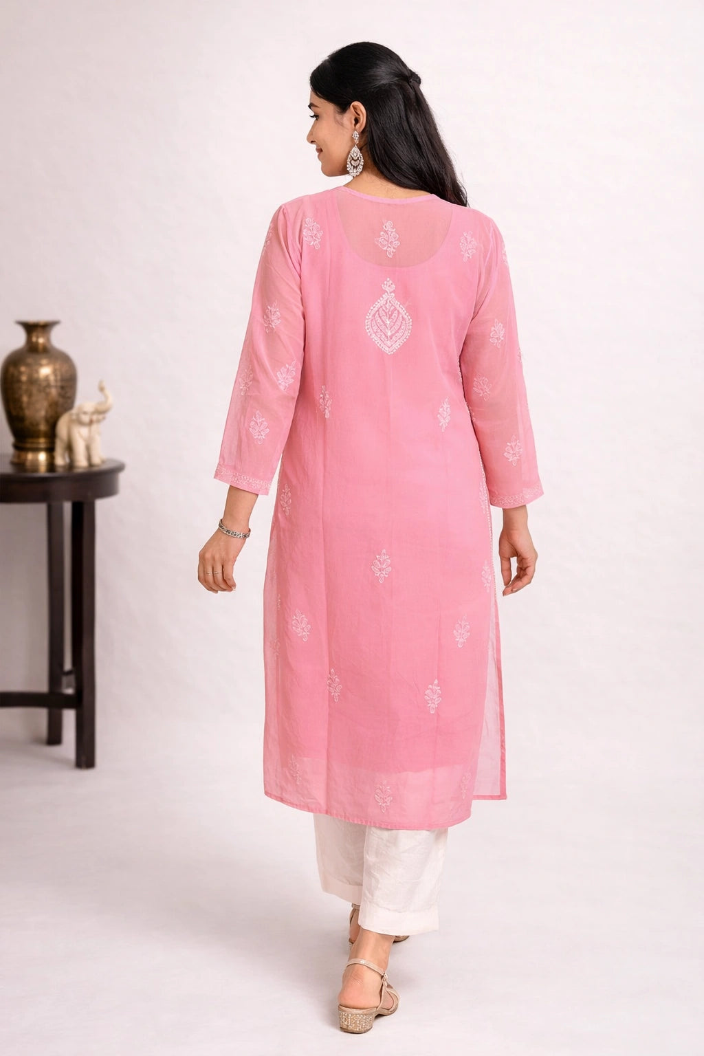Lucknowi chikankari A woman modeling a light pink kurta with white pants in a bright, modern studio setting with decorative white pedestals.