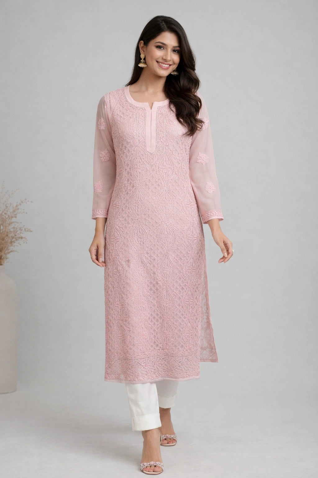 Woman wearing a lucknowi chikankari  pink kurta with white pants on a gray background