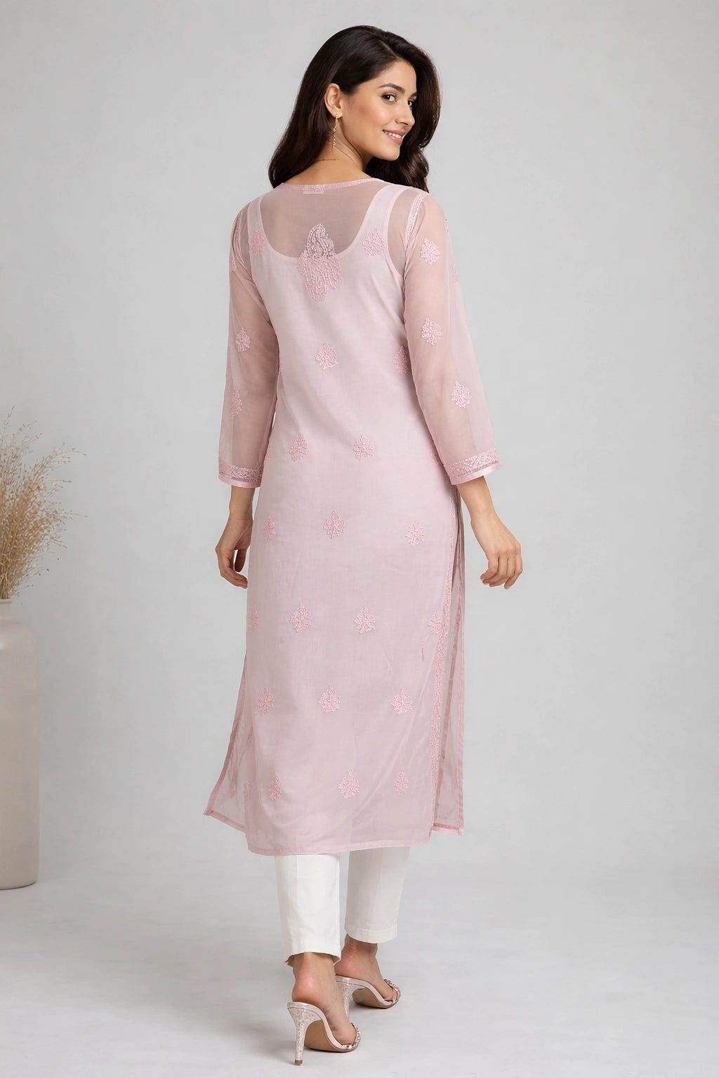 Woman wearing a lucknowi chikankari  light pink kurta with white pants on a plain background