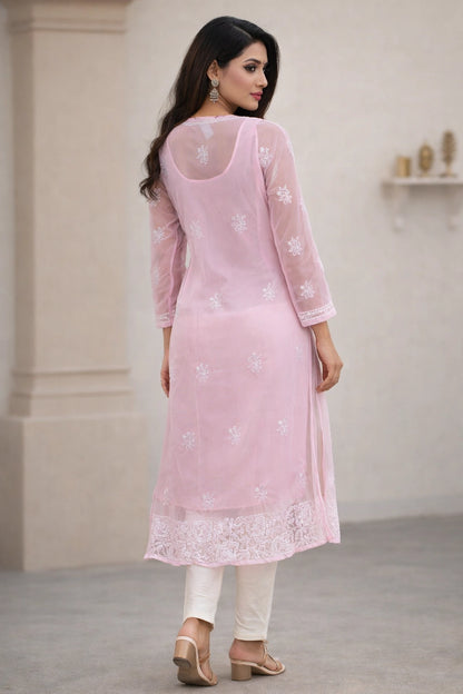 Woman wearing a light pink embroidered kurta with white pants in an indoor setting.