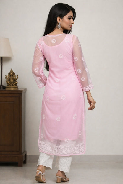 Woman wearing a lucknowi pink traditional outfit with white patterns against a plain background