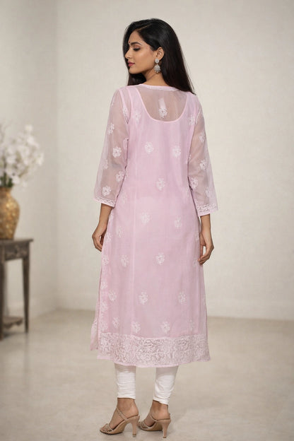 Woman wearing a light lucknowi chikankari pink kurta with white floral patterns in a minimalistic setting.
