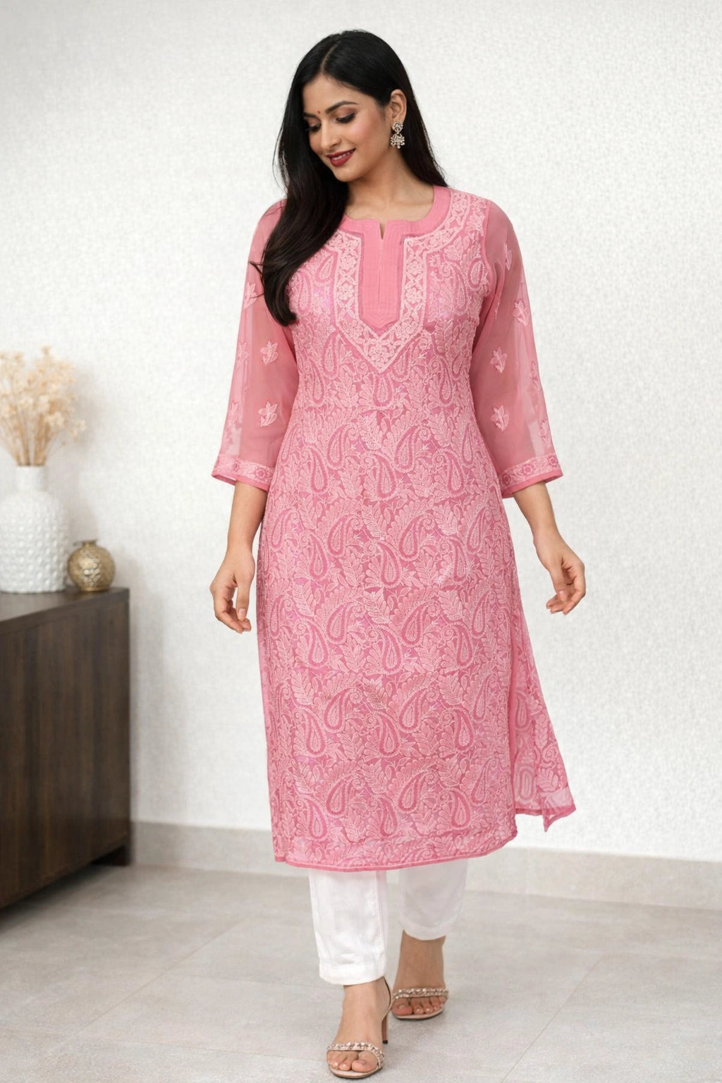 Woman wearing a pink embroidered kurta with white pants against a white background