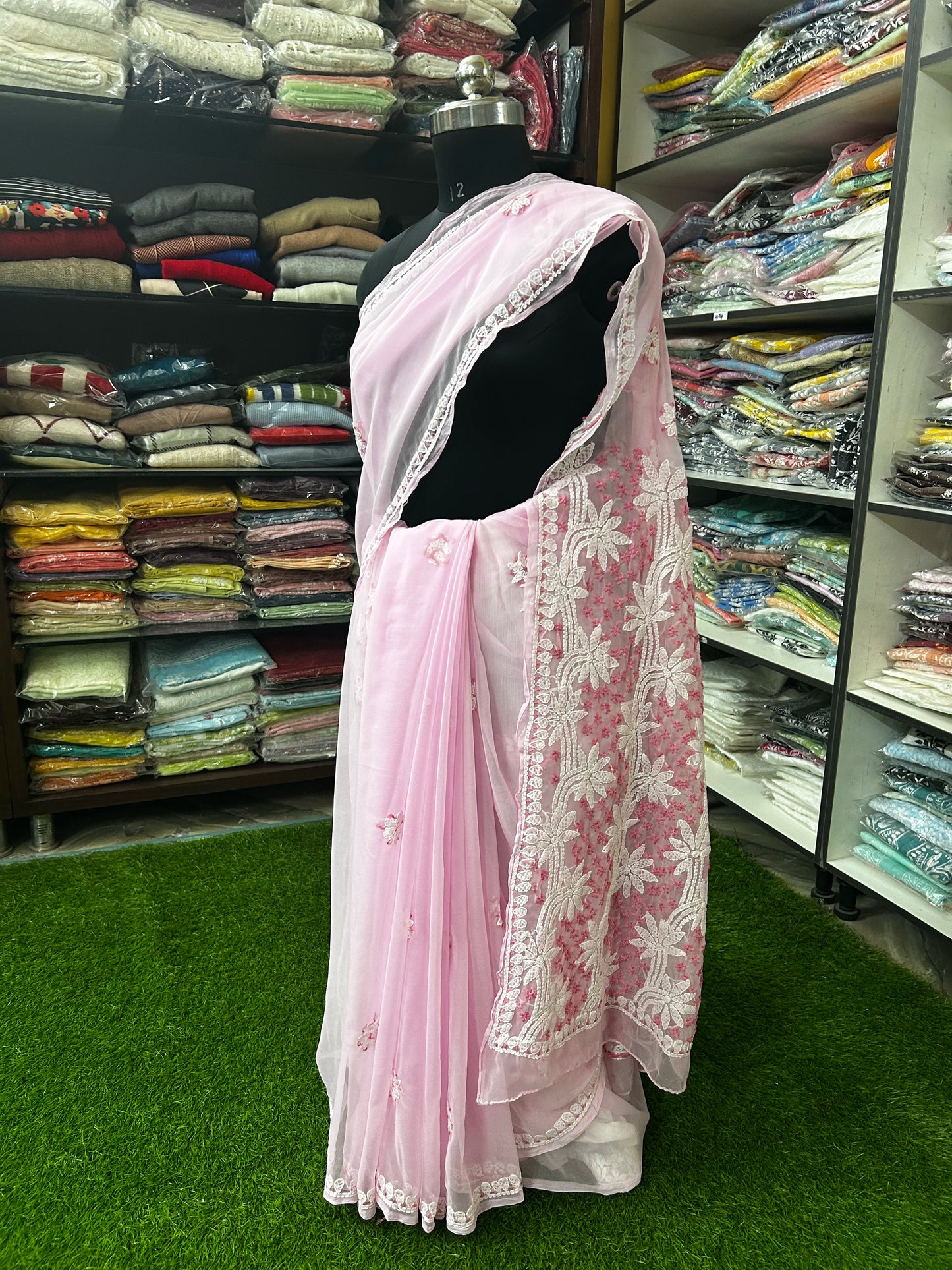 Mannequin wearing a lucknowi chikankari  pink saree with white floral patterns in a fabric store.