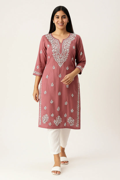 Woman wearing a pink embroidered kurta with white pants on a white background