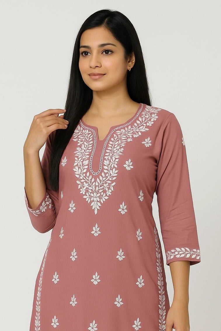 Woman wearing a pink kurta with white floral embroidery on a plain background