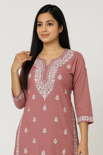 Woman wearing a pink kurta with white floral embroidery on a plain background