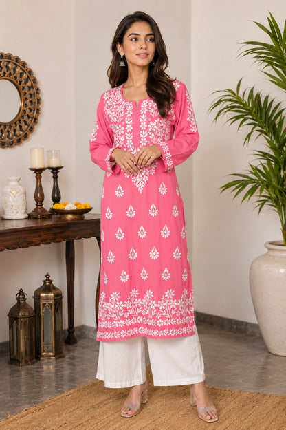 Woman wearing a pink embroidered kurta with white pants in a home setting.