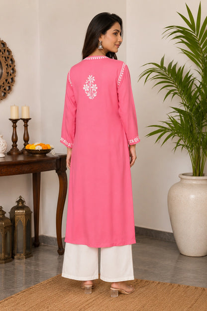 Woman wearing a pink kurta with white embroidery in a room with a table and plant.