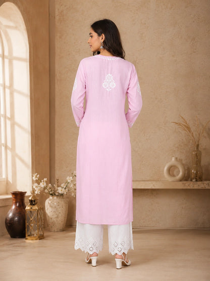 Woman wearing a pink kurta with white embroidery in a room with beige walls and decorative vases.