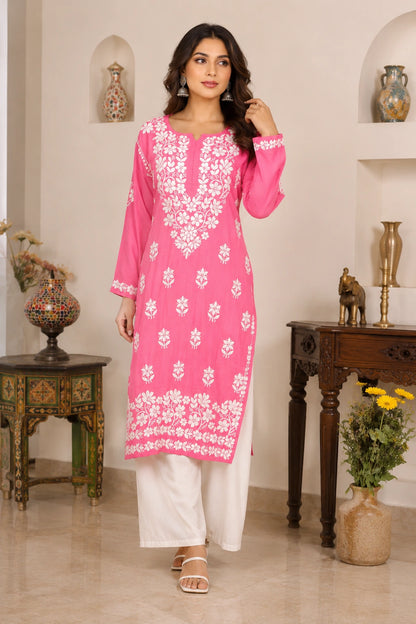 Woman wearing a pink embroidered kurta with white pants in an elegant indoor setting.
