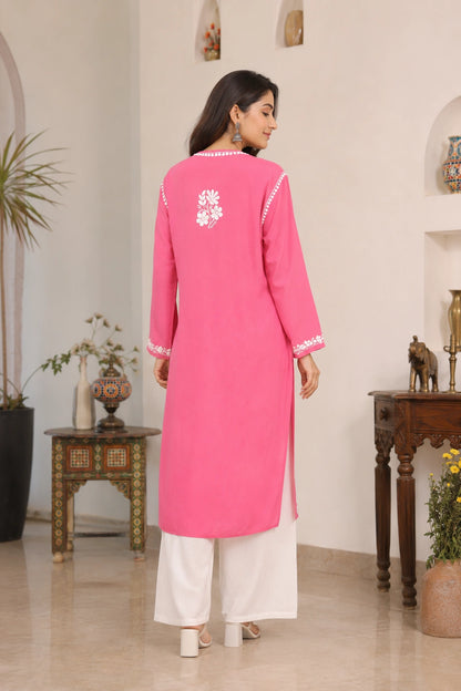Woman wearing a pink kurta with white embroidery in a decorated room.