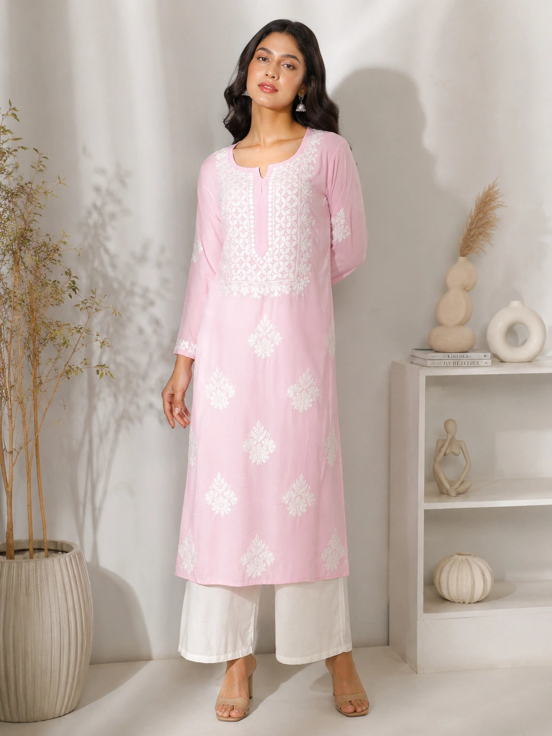 Woman wearing a pink kurta with white floral embroidery in a minimalistic room.