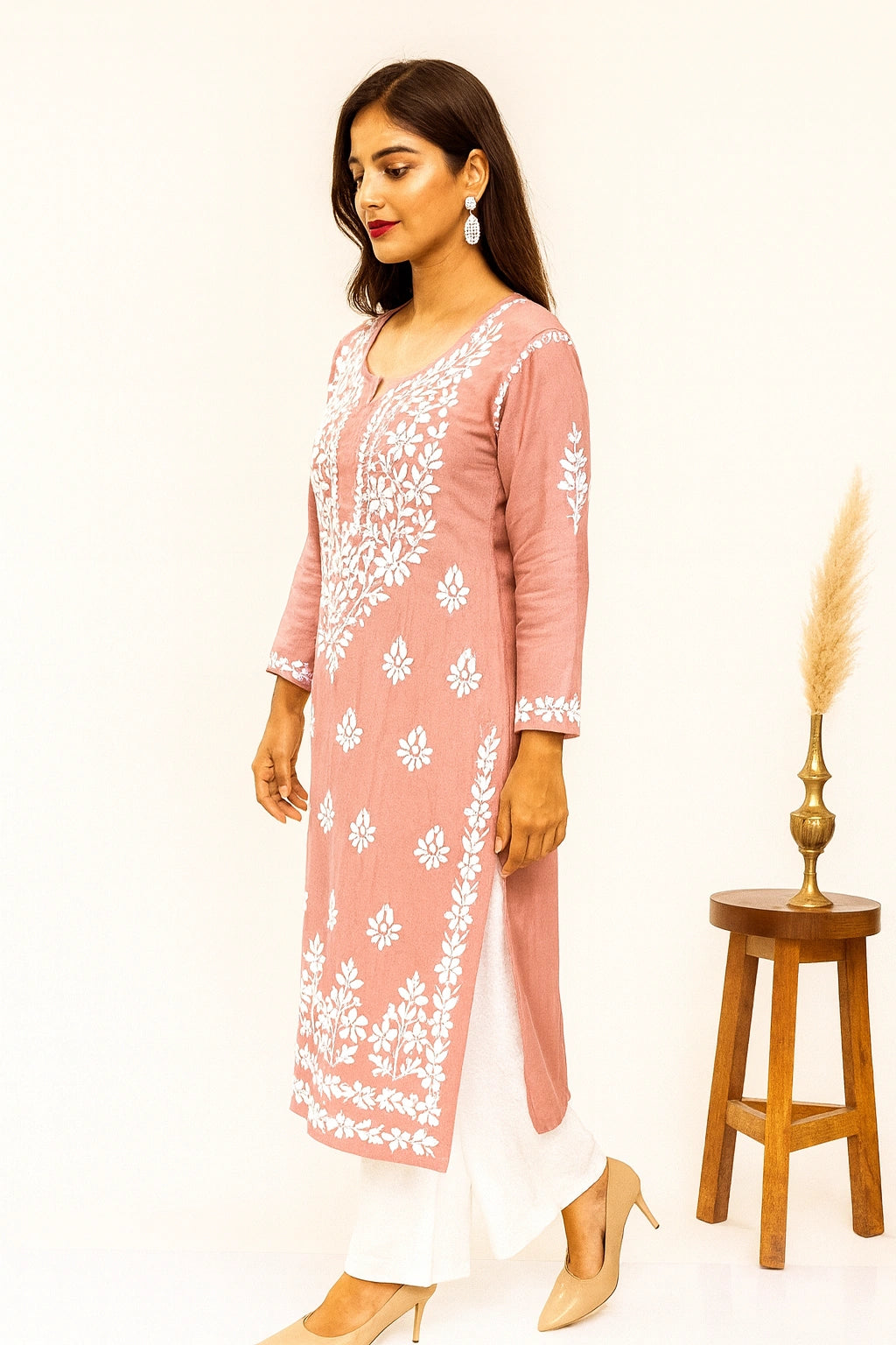 Woman wearing a pink embroidered kurta with white pants in an elegant indoor setting.