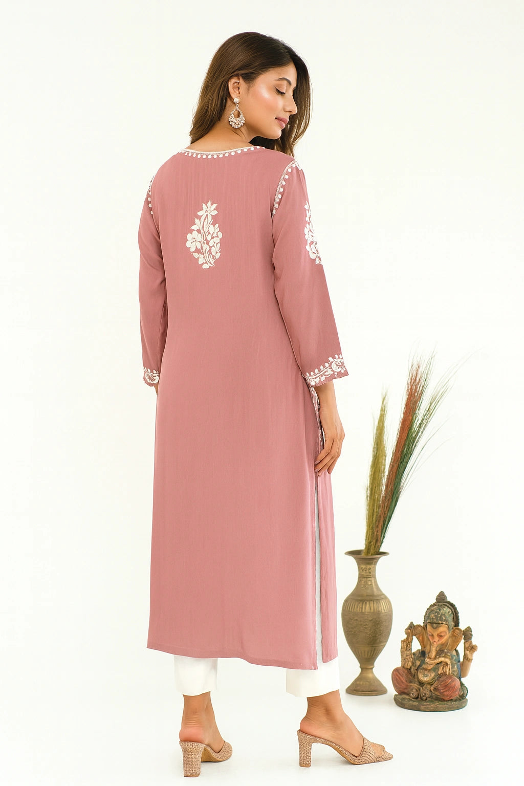 Woman wearing a pink kurta with white embroidery in a decorated room.