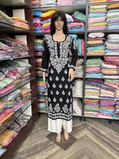 lucknowi chikankari Mannequin wearing a black and white patterned outfit in front of shelves filled with colorful fabrics.