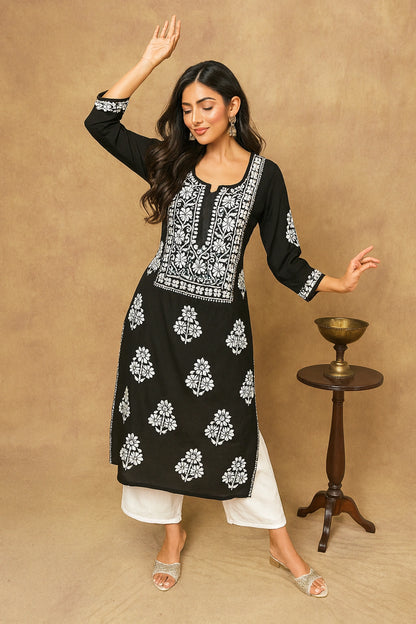 Woman wearing a black and white embroidered kurta with white pants against a beige background