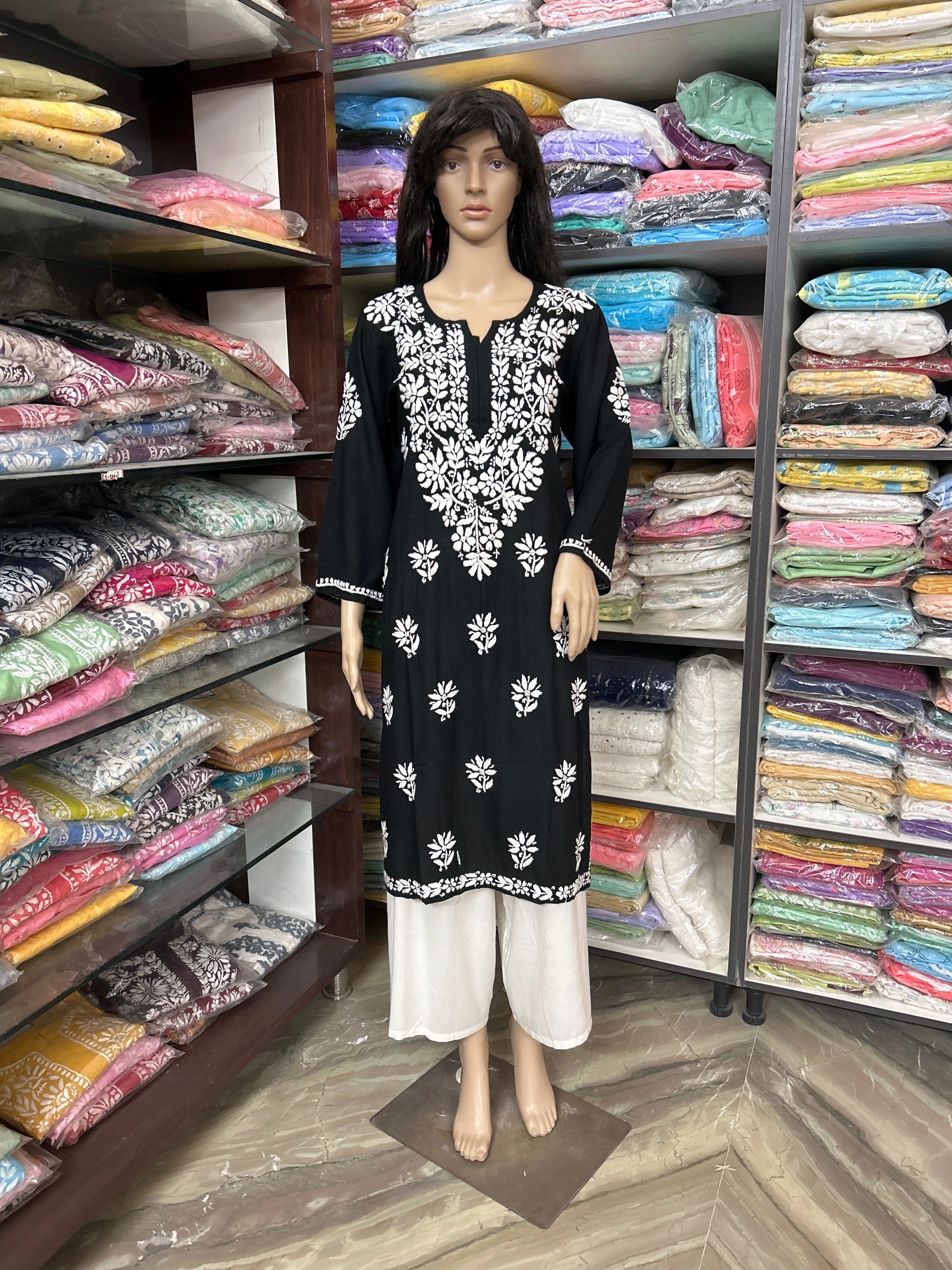 lucknowi chikankari Mannequin wearing a black and white patterned dress in front of shelves filled with colorful fabric.