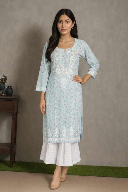 A woman modeling a light blue embroidered kurta with white flared pants, standing against a textured gray wall.